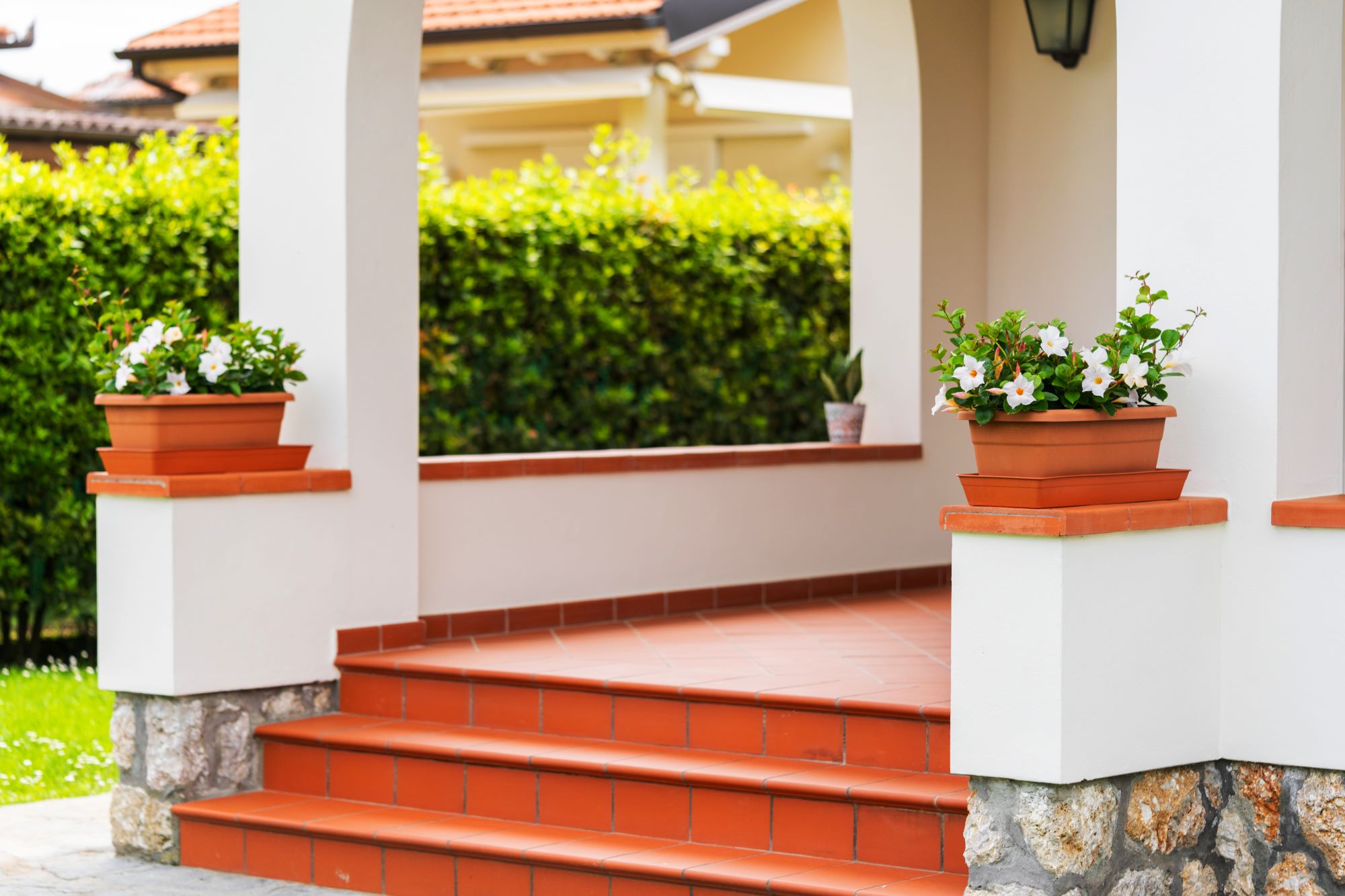 A front porch with red tiled steps, two potted plants on columns, and green shrubbery in the background sets a charming scene reminiscent of an Auto Draft blueprint come to life.